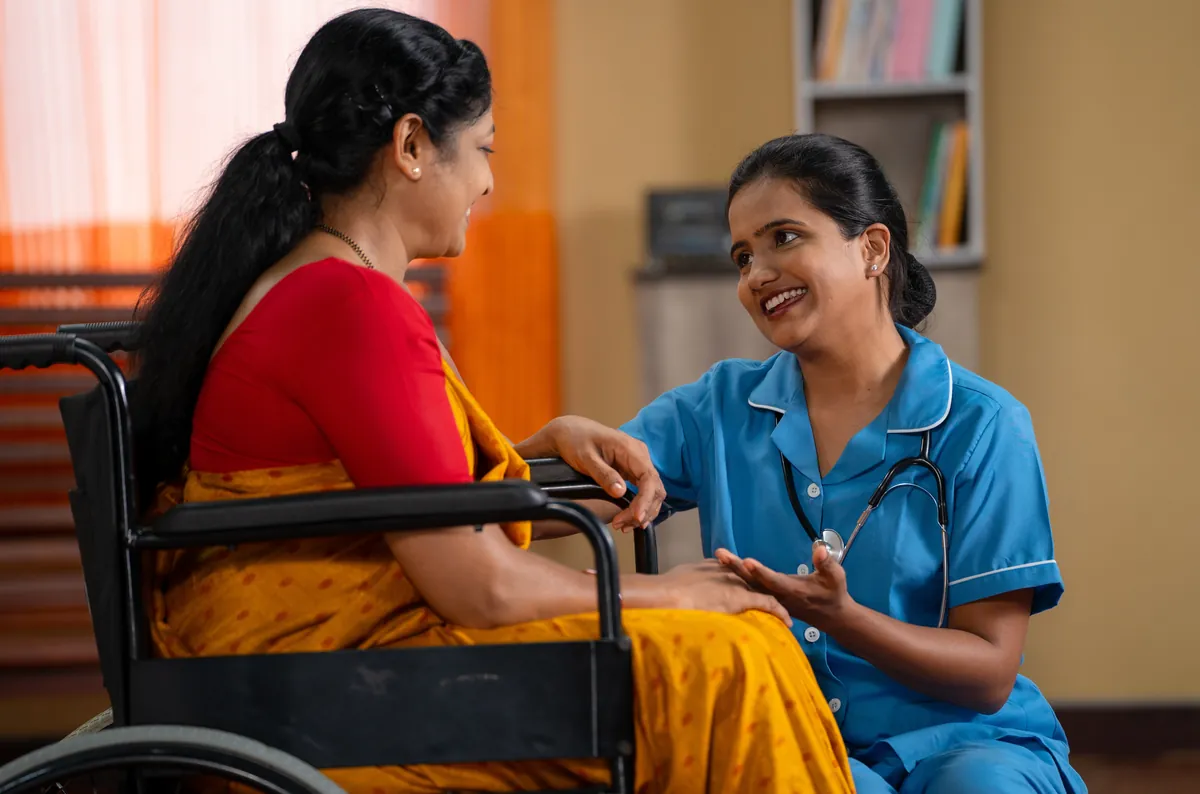 Smiling carer in blue uniform with an older woman in a wheelchair