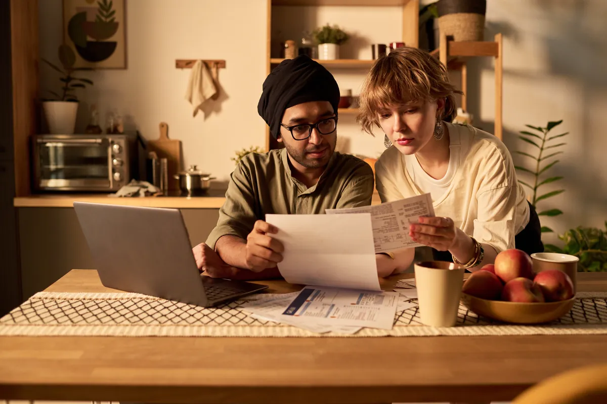Couple reviewing documents beside a laptop at a kitchen table