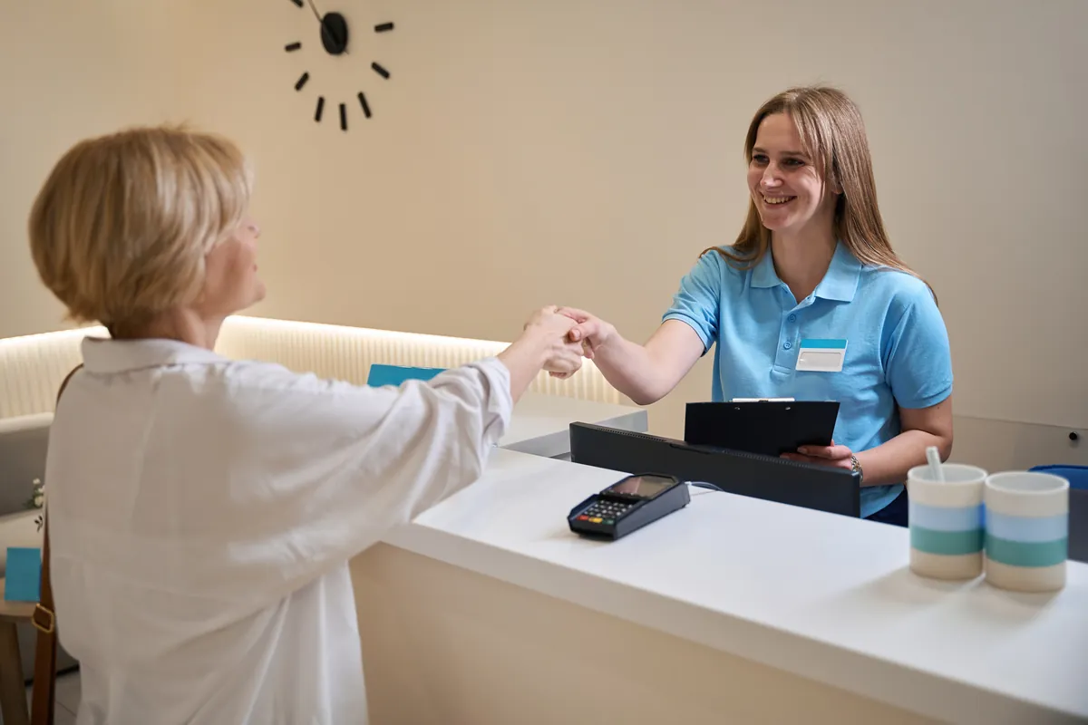 Smiling receptionist greeting a visitor at a bright white reception desk