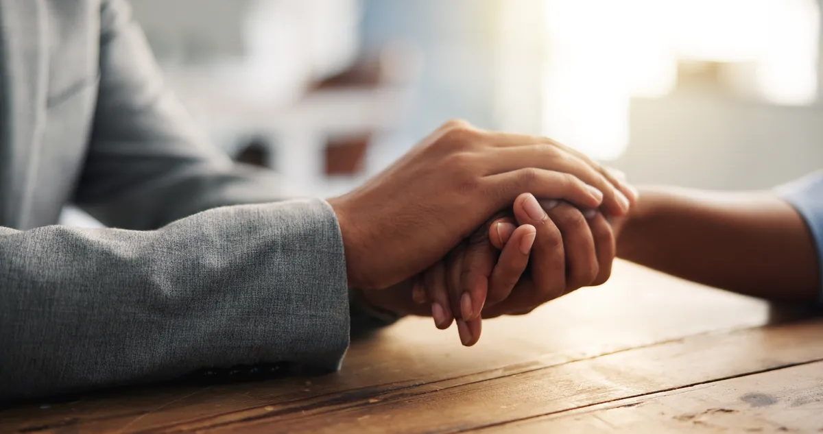 Two people holding hands across a table in support