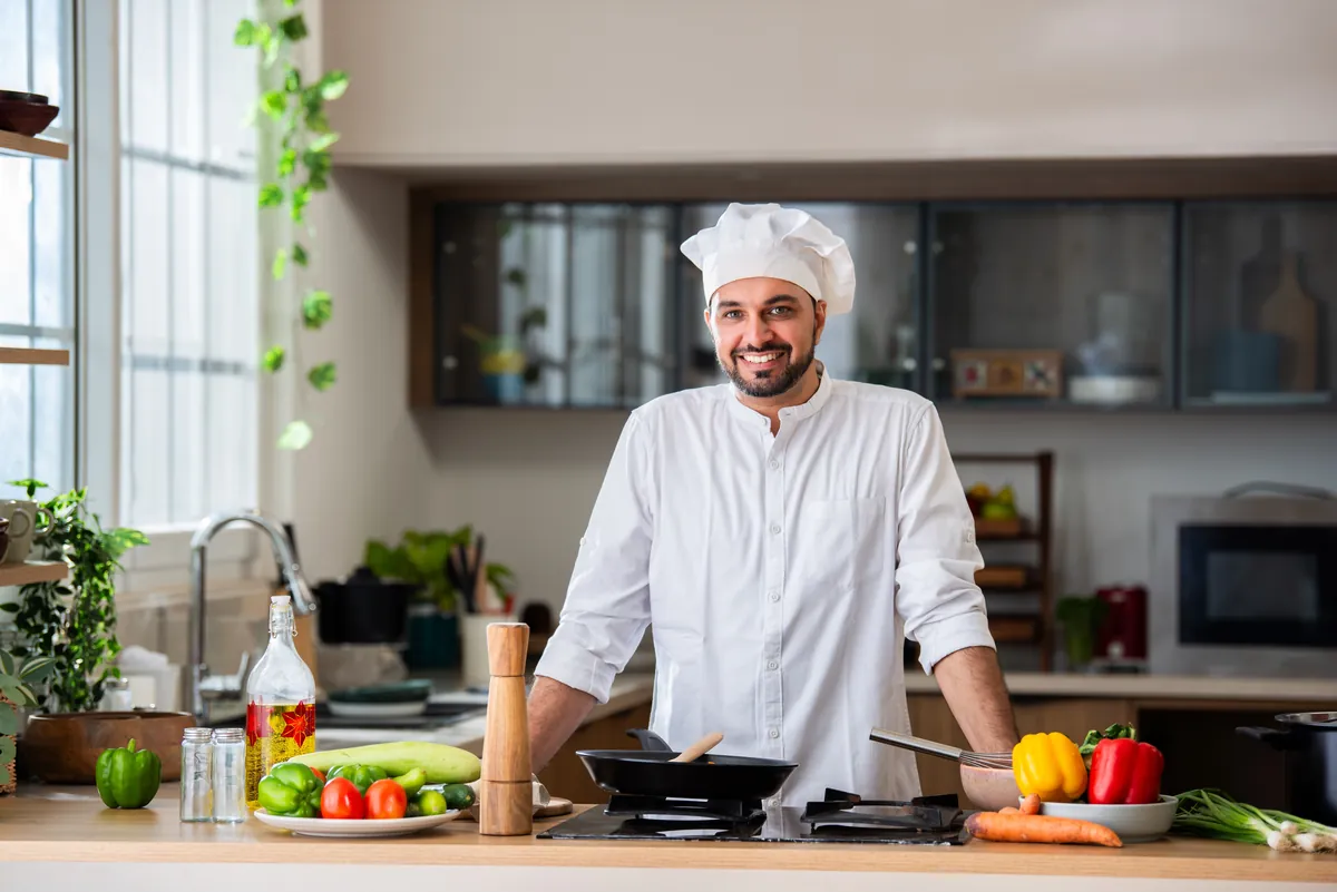 Smiling Indian chef in whites cooking in a bright kitchen