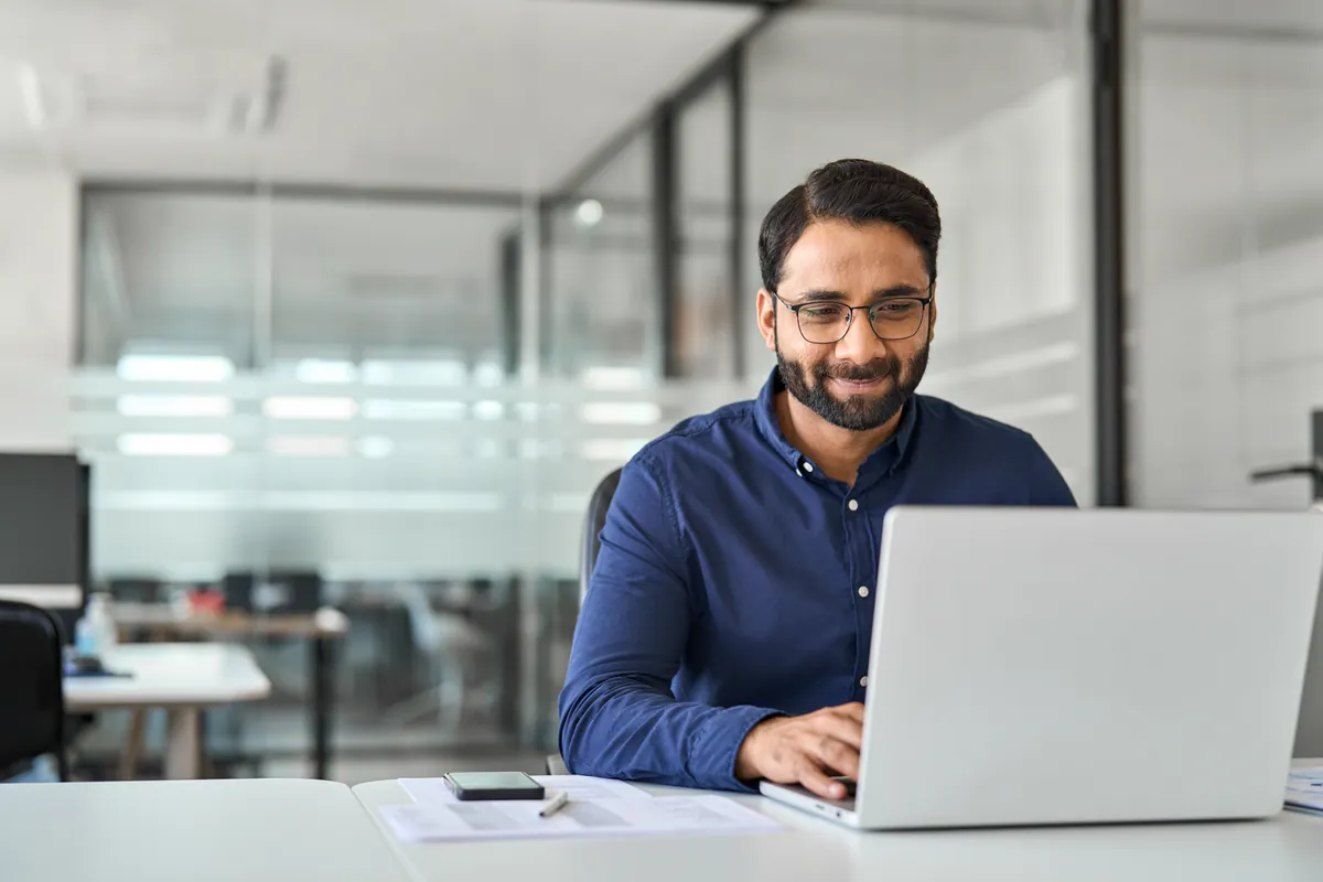 Smiling Indian IT professional working on a laptop in a bright office