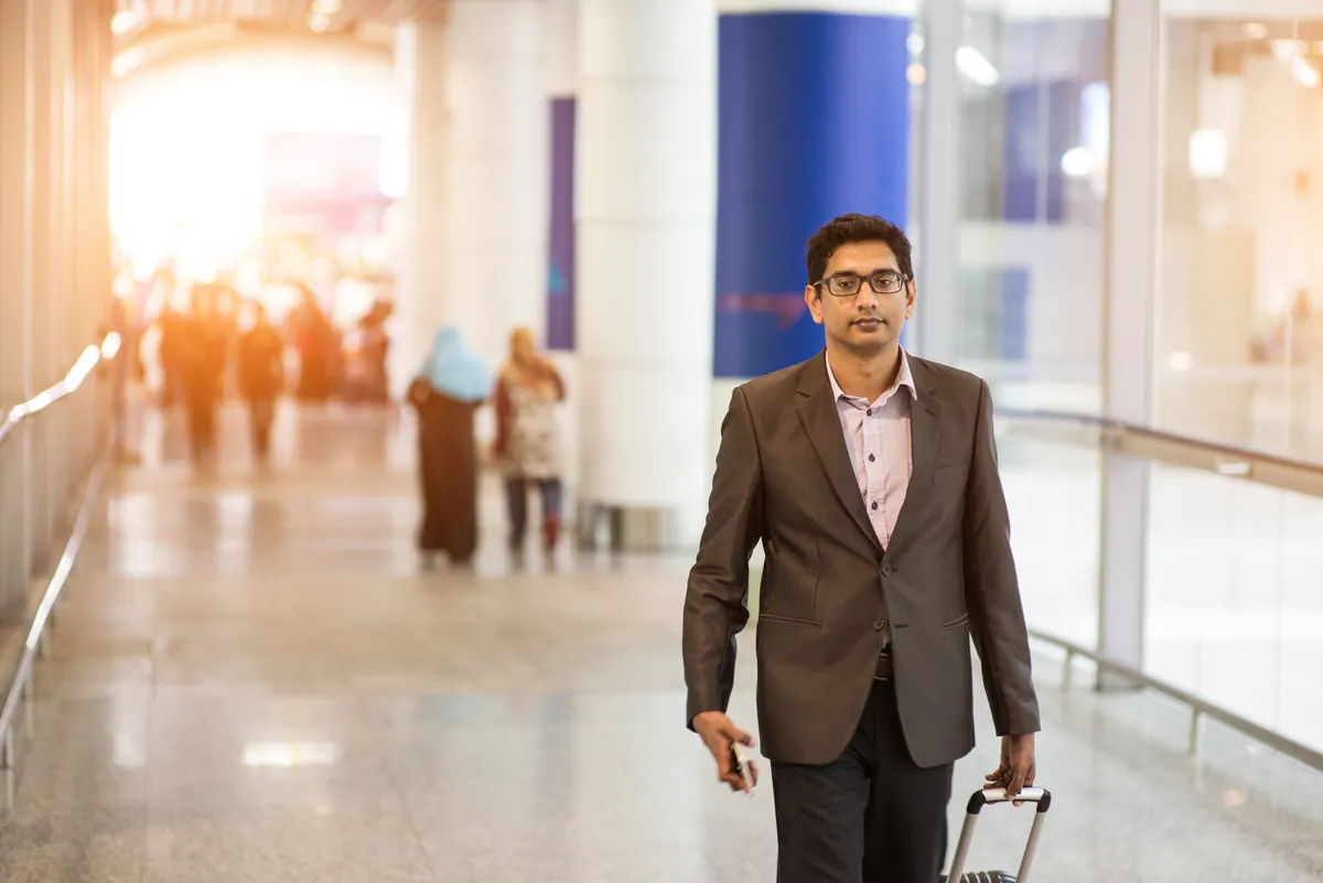 Smiling man pulling a suitcase through a bright airport terminal