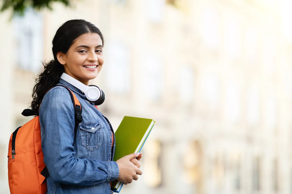 Smiling Indian student with backpack and books on a sunny campus