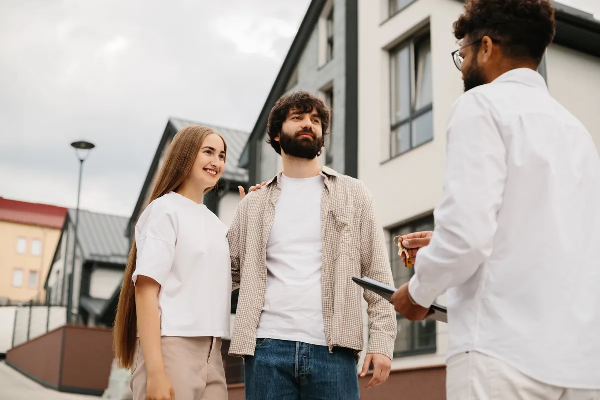 Young couple receiving keys from an agent outside a modern apartment block