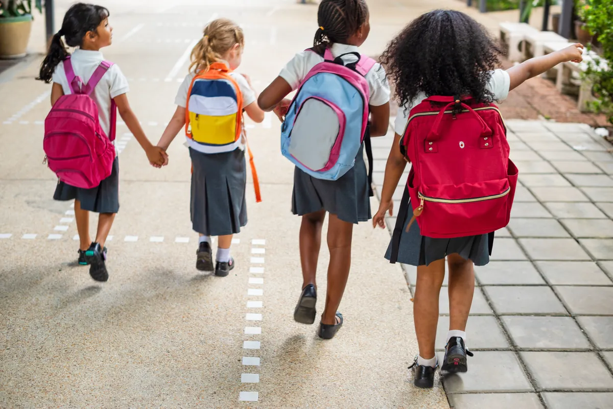 Primary school children with backpacks walking hand in hand, seen from behind