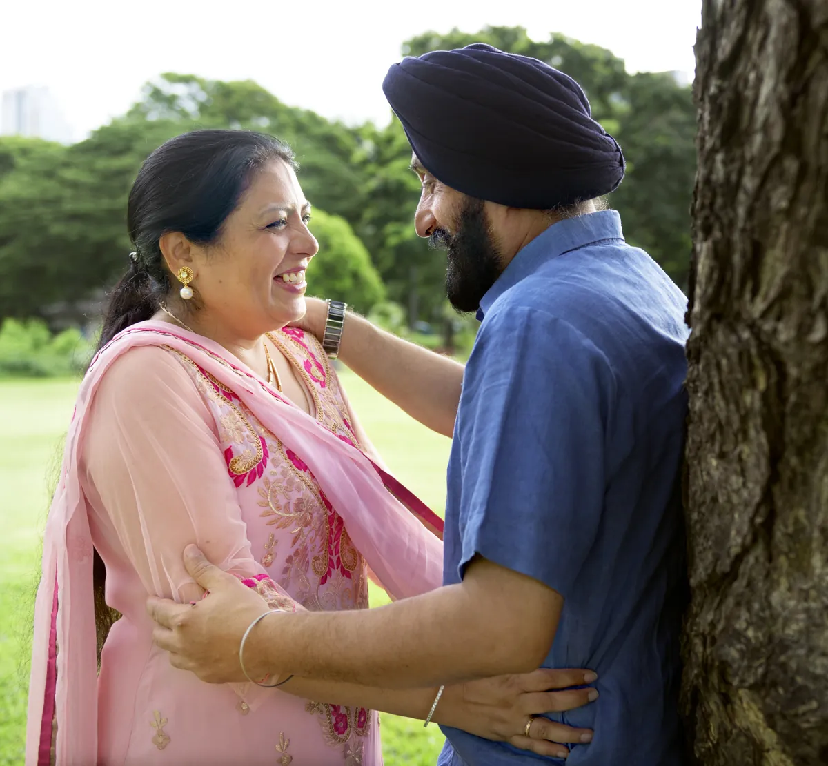 Older Sikh couple sharing a warm embrace in a leafy park
