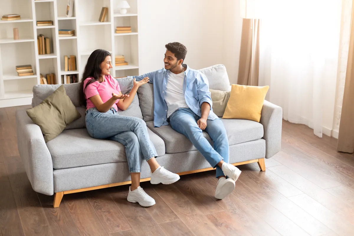 Young South Asian couple chatting on a sofa in a bright living room
